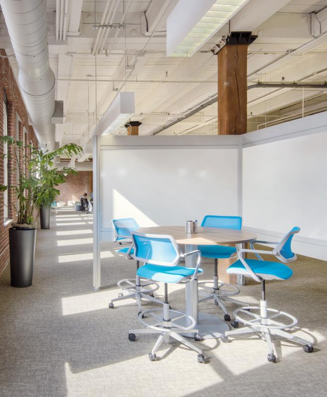 Partitioned meeting area with open office beyond, with row of windows in brick wall