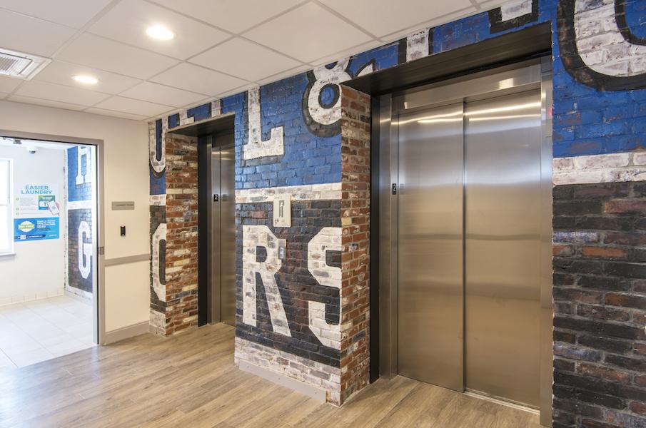 Elevator lobby; brick wall covered by mural with large lettering.