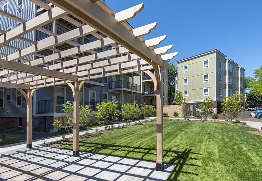 Wooden pergola and lawn behind buildings.