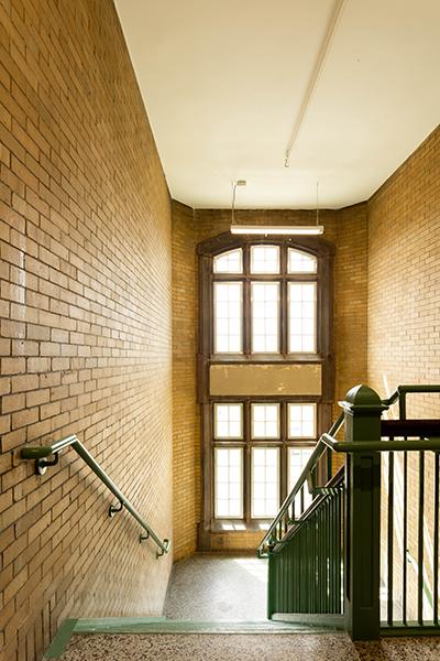 Historic stairwell with tall windows and brick walls.
