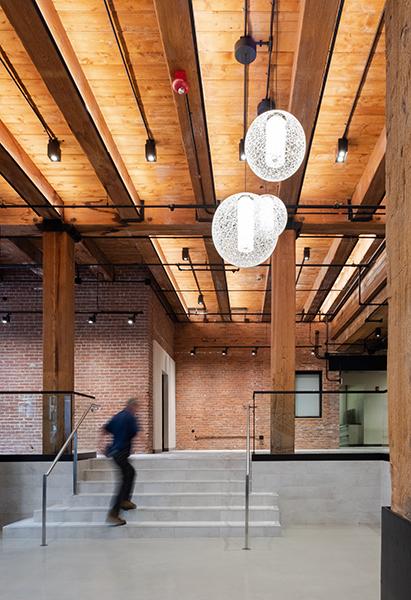 Wide stair from lobby up to higher-level area with brick walls and wooden ceiling.